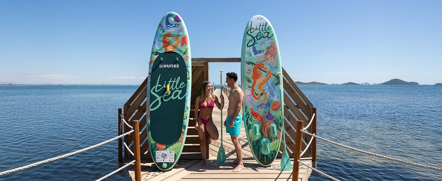 Zwei dekorative Paddelbretter mit tropischen Motiven auf einem Holzsteg mit Blick auf das ruhige Meerwasser mit fernen Inseln.